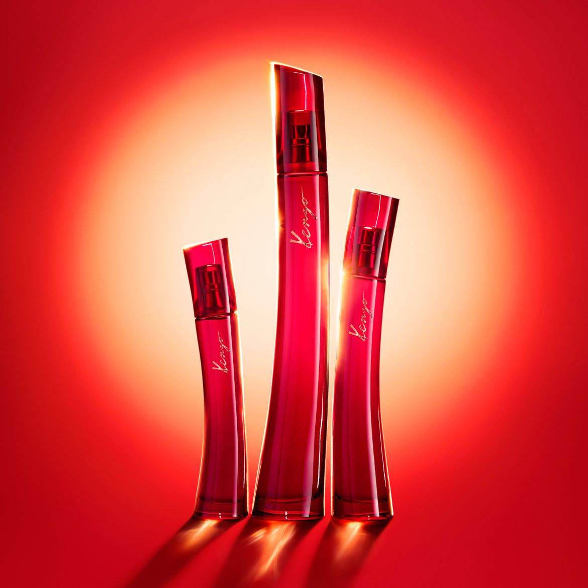 Trois bouteilles de parfum Kenzo rouge rubis se dressent sur un fond rouge éclatant, leurs silhouettes élégantes captant la lumière.