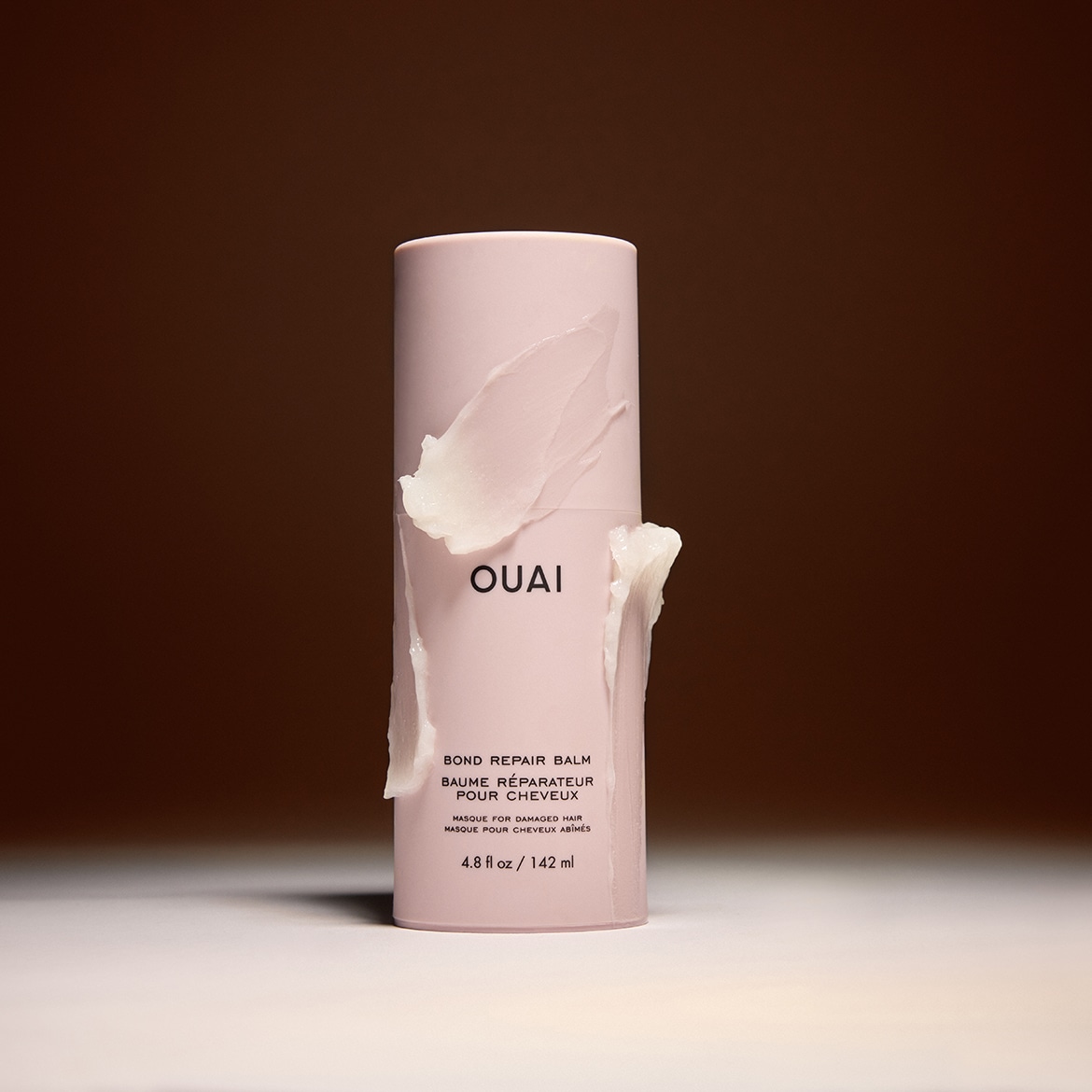 Roze tube van OUAI Bond Repair Balm, een herstellende haarmasker voor beschadigd haar, met een inhoud van 142 ml, versierd met een witte crème.