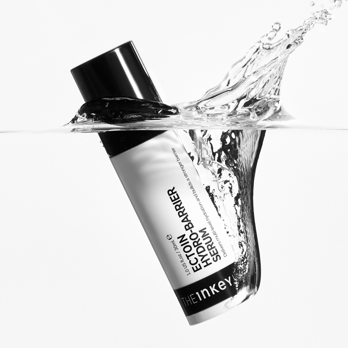 De Inkey List Ectoin Hydro-Barrier Serum, verpakt in een witte tube met zwarte dop, wordt omgeven door opspattend water, wat de hydraterende werking benadrukt.