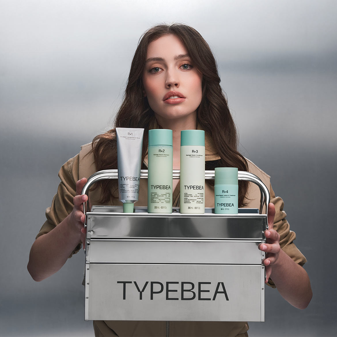 Une femme tient un chariot métallique contenant les produits capillaires TYPEBEA : un masque, un shampooing, un revitalisant et un soin sans rinçage.
