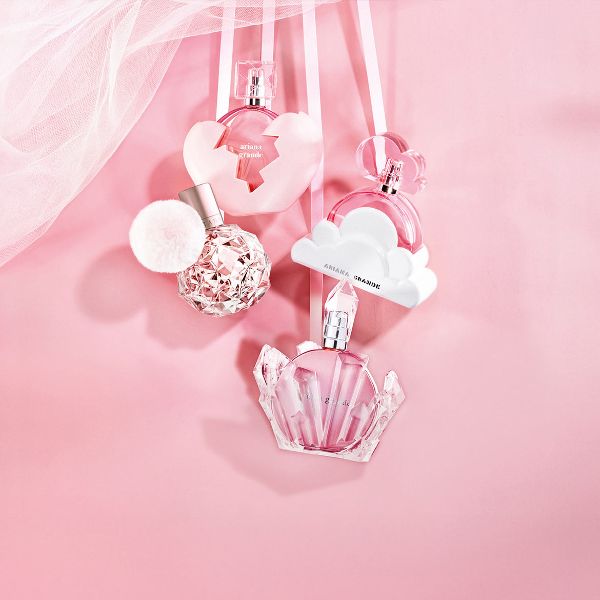Découvrez un assortiment de parfums Ariana Grande, chacun dans un flacon unique : cœur brisé, sphère à pompon, nuage et cristal, suspendus sur un fond rose doux.