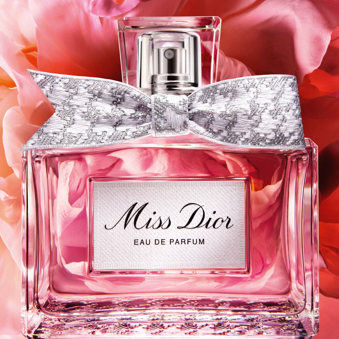 De Miss Dior Eau de Parfum is een roze vloeistof in een glazen fles met een zilveren strik en een wit etiket met zwarte letters, omringd door roze bloemblaadjes.