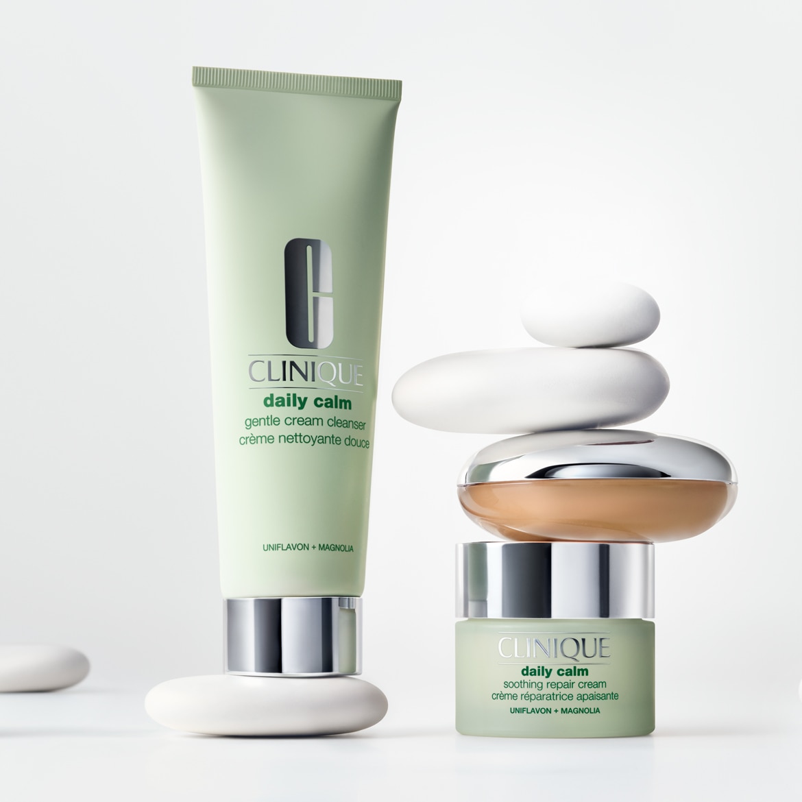 De Clinique Daily Calm Gentle Cream Cleanser en Soothing Repair Cream, beide in lichtgroene verpakkingen, staan opgestapeld met witte stenen, wat een gevoel van rust en balans oproept.