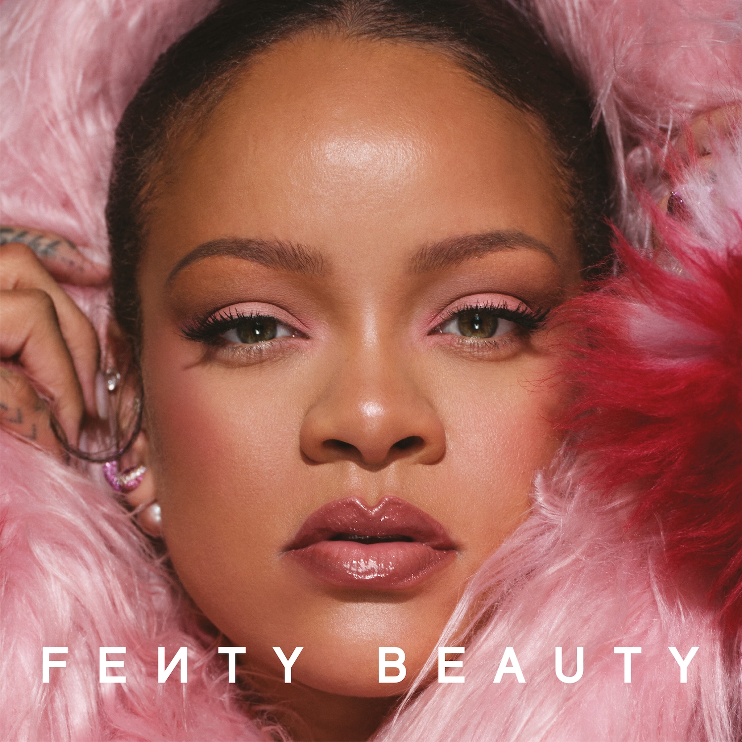 Een close-up van Rihanna omringd door roze veren, met een zachte roze make-up en glanzende lippen, met de tekst "Fenty Beauty".