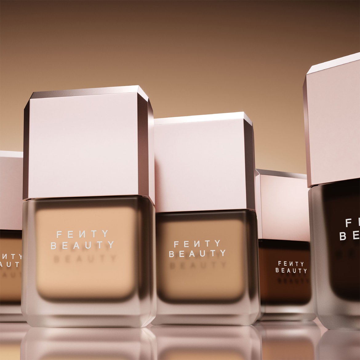 Flacons de fond de teint Fenty Beauty dans une gamme de teintes, du clair au foncé, avec une finition en verre mat et un capuchon rose pâle brillant.