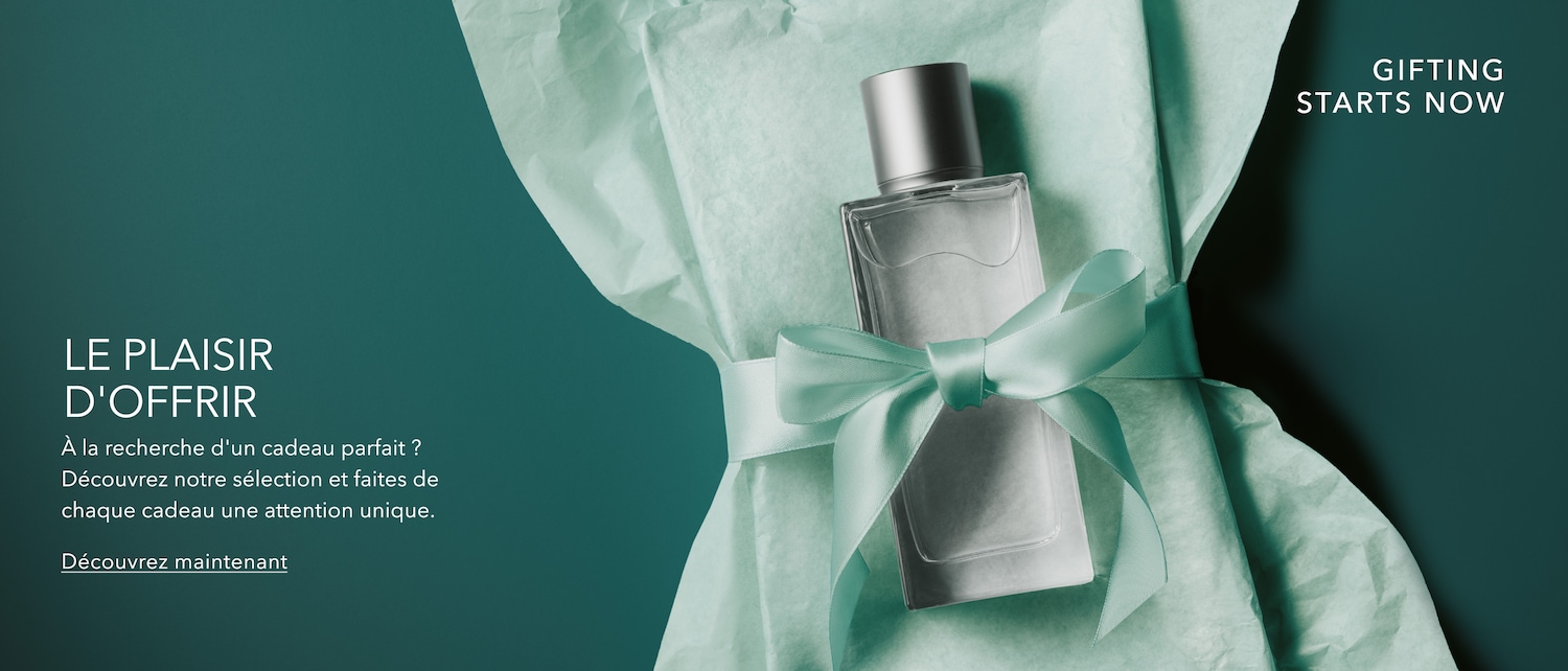 Un flacon de parfum avec un bouchon argenté et un nœud bleu clair, entouré de papier de soie bleu clair, avec le texte "GIFTING STARTS NOW" et "LE PLAISIR D'OFFRIR".