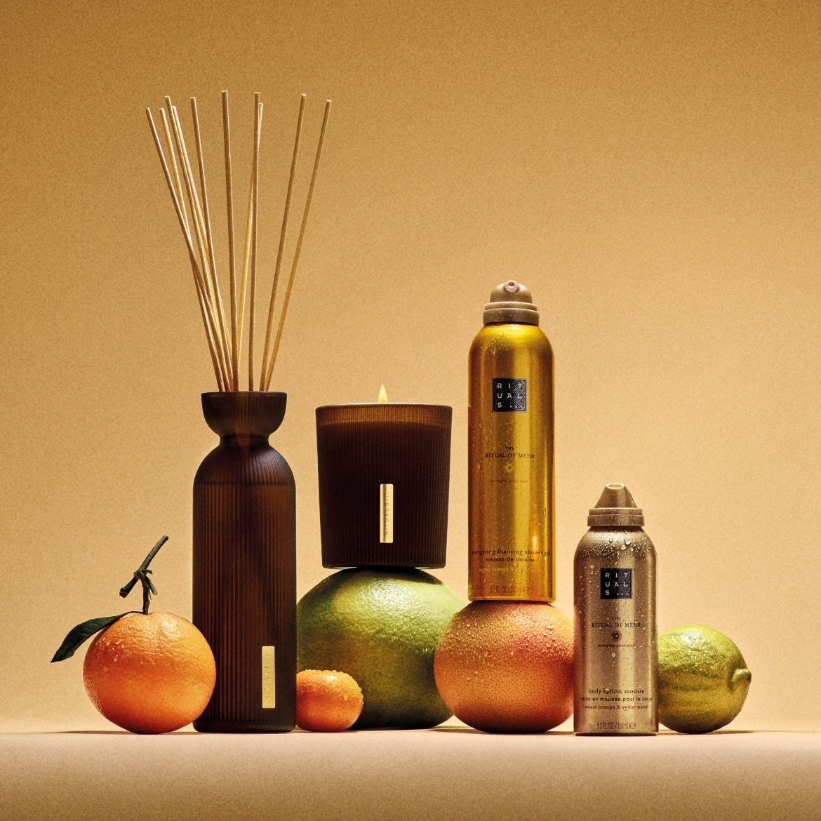 Découvrez l'élégance avec Ritual of Mehr : diffuseur de parfum brun, bougie, mousse de douche dorée et lotion pour le corps, présentés avec des agrumes frais.