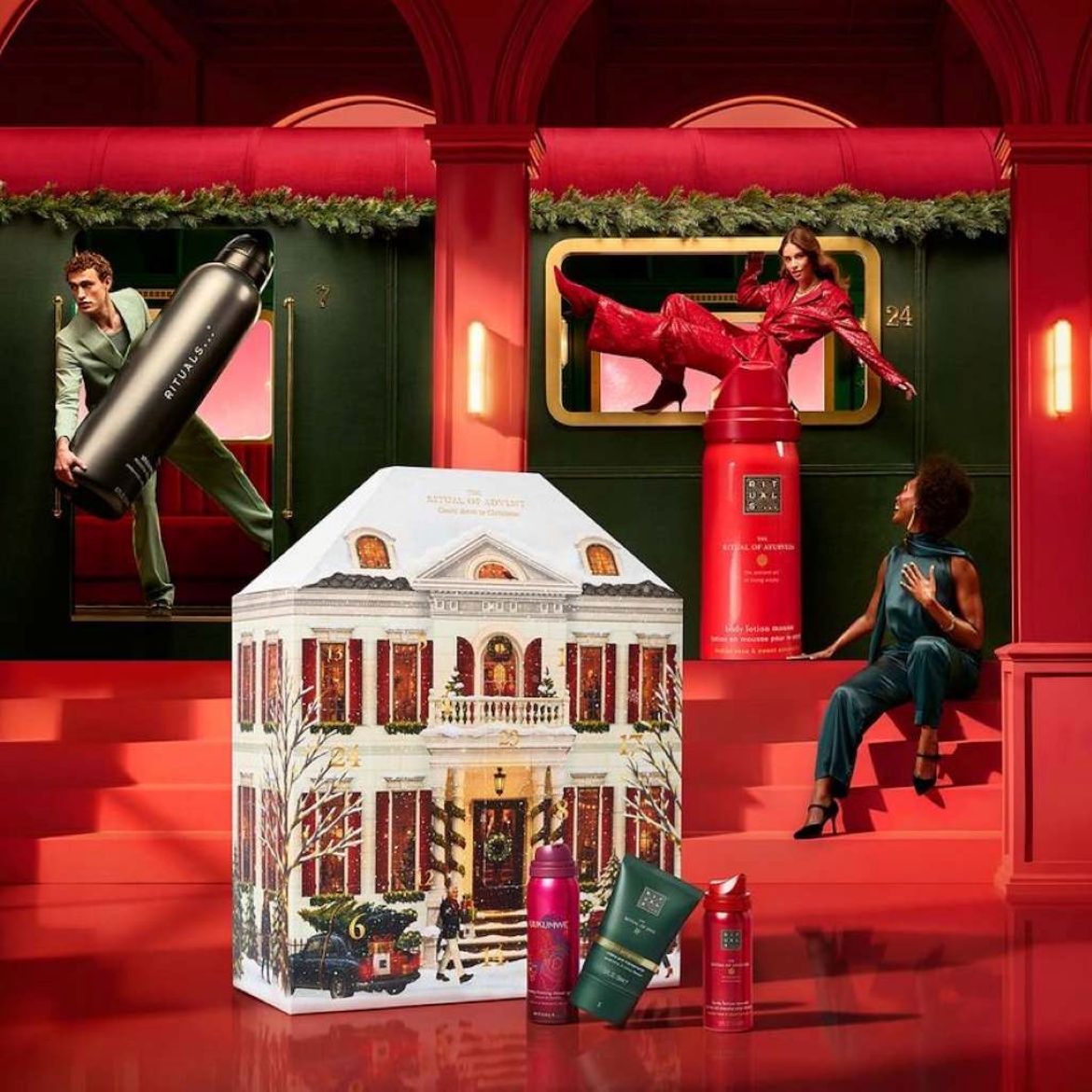 Calendrier de l'Avent Rituals 2023 : un design de maison festif avec 24 surprises luxueuses, entouré de mannequins et de produits Rituals dans un décor rouge rappelant un train.