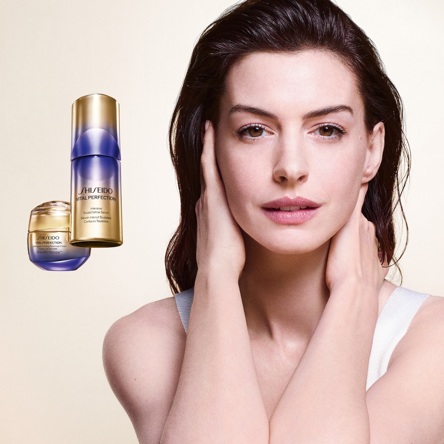 Een vrouw met donkerbruin haar en een lichte huid raakt haar gezicht aan, met op de achtergrond twee Shiseido Vital Perfection producten: een crème en een serum in paarse en gouden verpakkingen.