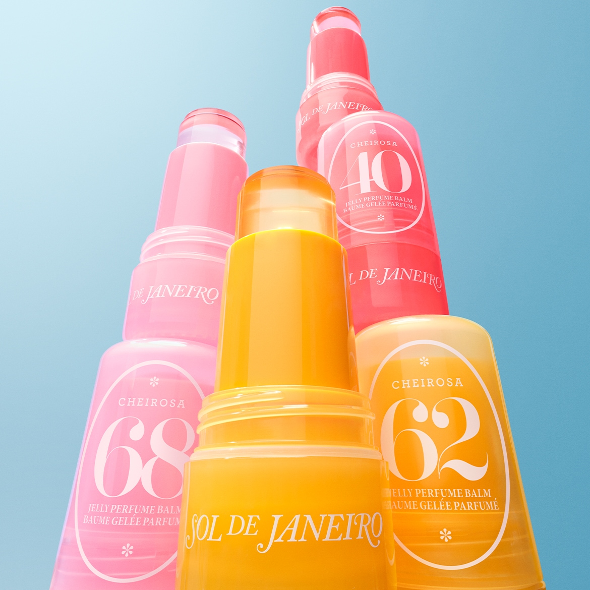 Stapel kleurrijke Sol de Janeiro Cheirosa Jelly Perfume Balms, waaronder geel nr. 62, roze nr. 68 en rood nr. 40, tegen een blauwe achtergrond.