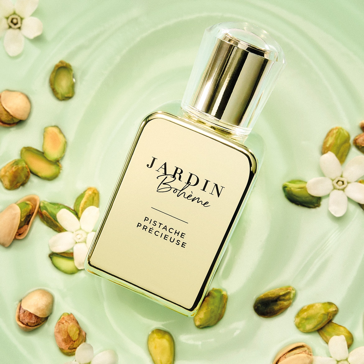 Jardin Bohème Pistache Précieuse Eau de Parfum, een elegante geur in een rechthoekige fles met gouden accenten, omringd door pistachenoten en witte bloesems op een lichtgroene achtergrond.