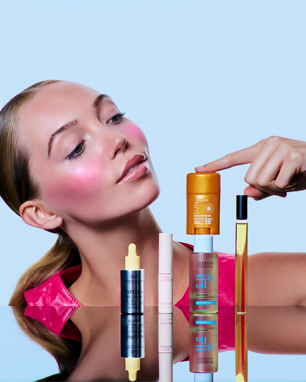 Ontdek een reeks schoonheidsproducten, waaronder TYPEBEA G-1, Kylie Cosmetics Wisp Lash en Douglas Essential make-upremoverolie, gepresenteerd op een reflecterend oppervlak.